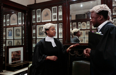 Two black barristers in wig and gown talking on a flight of stairs.